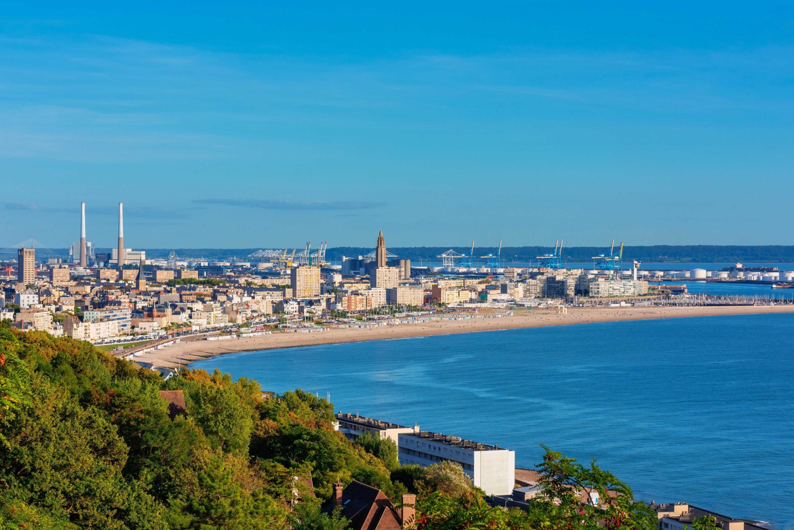 Coastline and harbor of Le Havre in Normandy with sandy beach under a blue sky curving along cityscape.