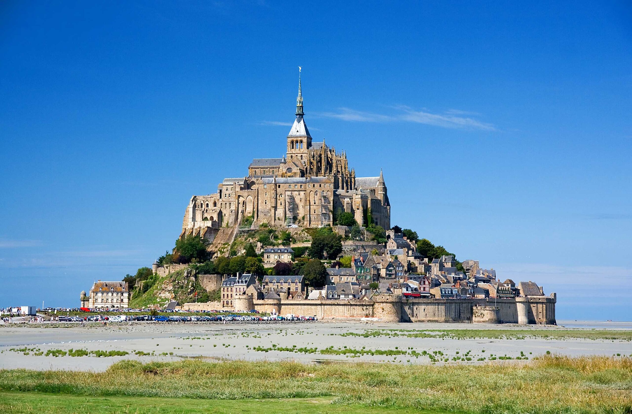 View of Mont-Saint-Michel Abbey from the bay with its Gothic spires rising up to meet the clear blue sky.