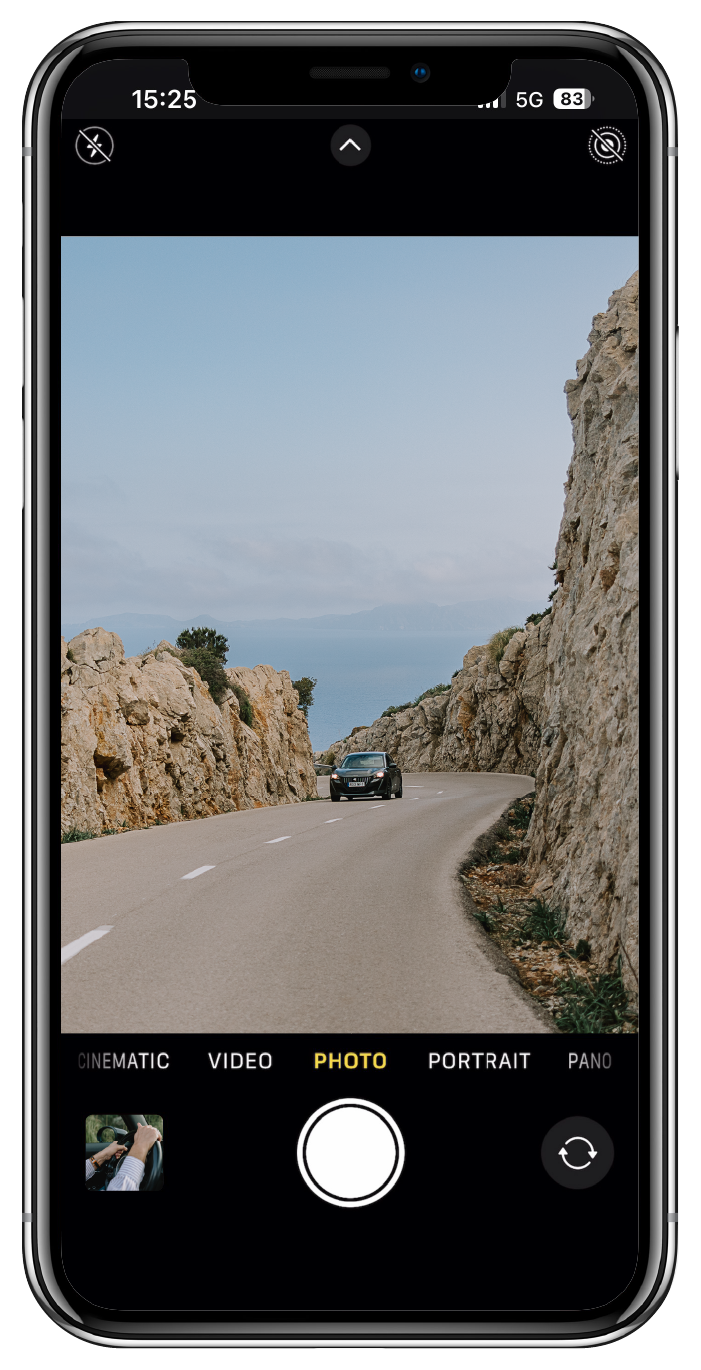 Smartphone displaying the camera app with a car driving between large beige rock formations on a winding road.