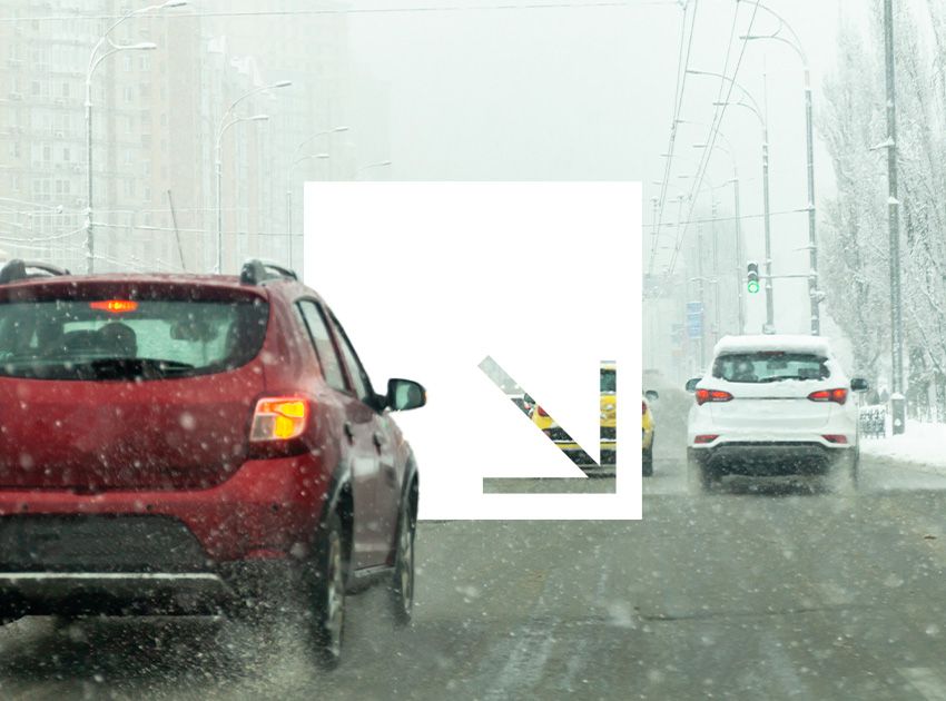 Cars driving through heavy snow on a city road with low visibility.