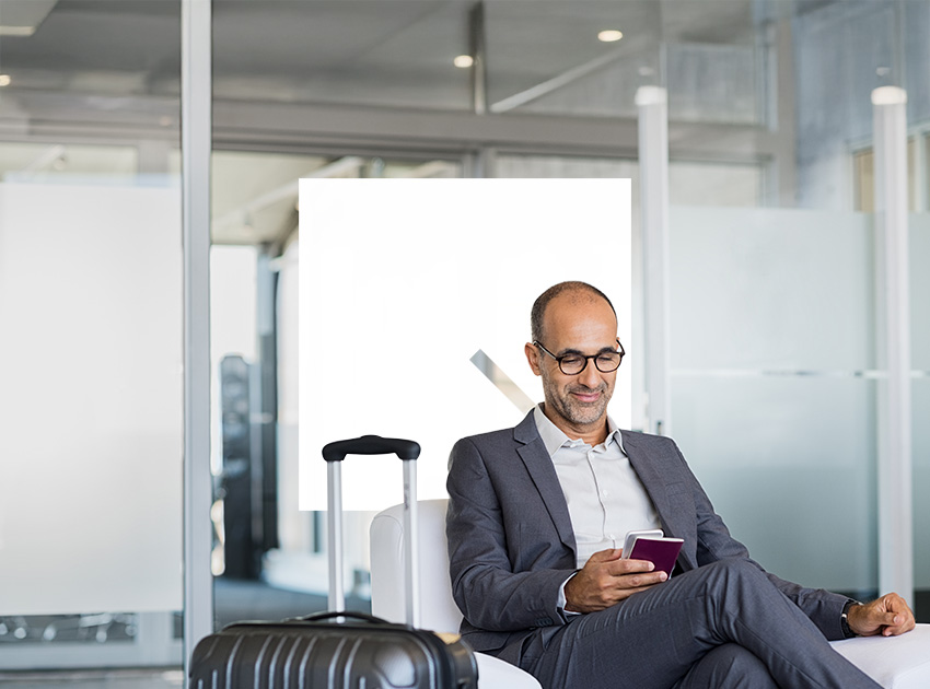 Business traveller sitting in an airport lounge checking his phone, reflecting situations where car hire excess insurance can help after travel disruption.