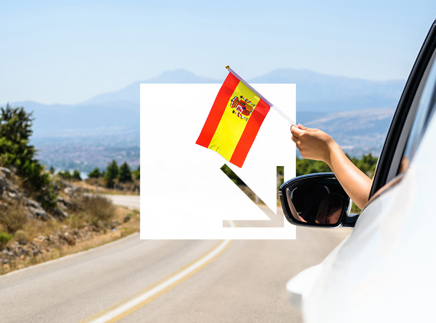 Hand holding a Spanish flag out of a car window on a rural road, representing driving abroad with car hire excess insurance.