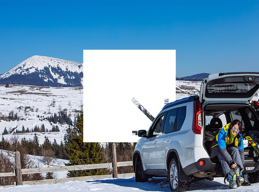 Driver sitting by an SUV in a snowy mountain area fitting ski boots, emphasising the value of car hire excess insurance during winter rentals.