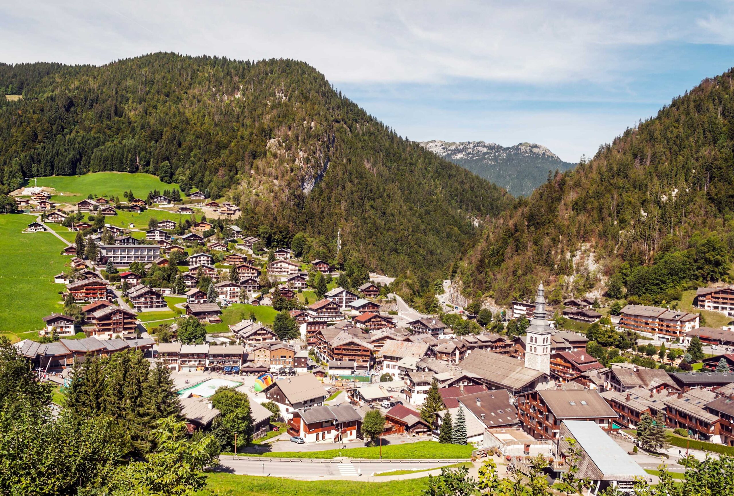 The alpine village of Megève featuring clustered wooden houses and a church steeple surrounded by forested hills.