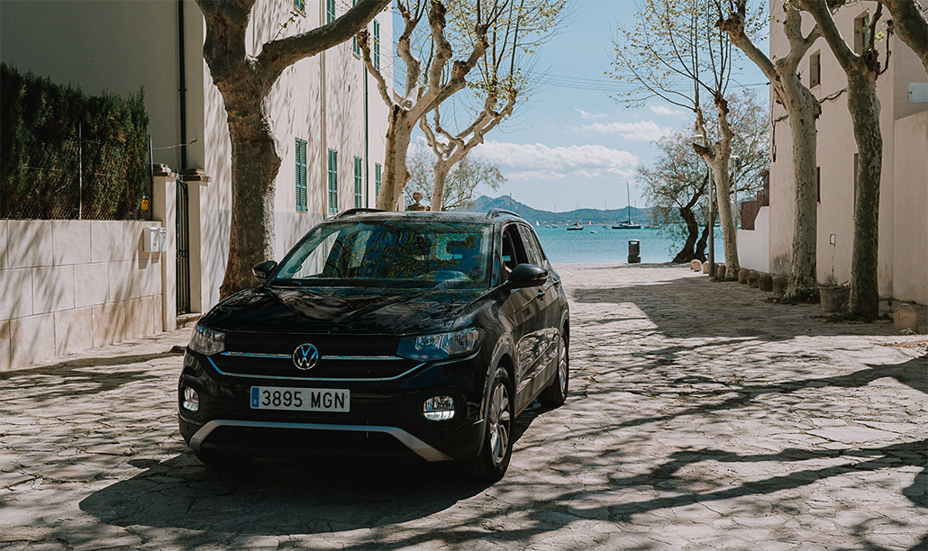 A black Volkswagen SUV is parked on a sunlit cobblestone street lined with leafless trees.