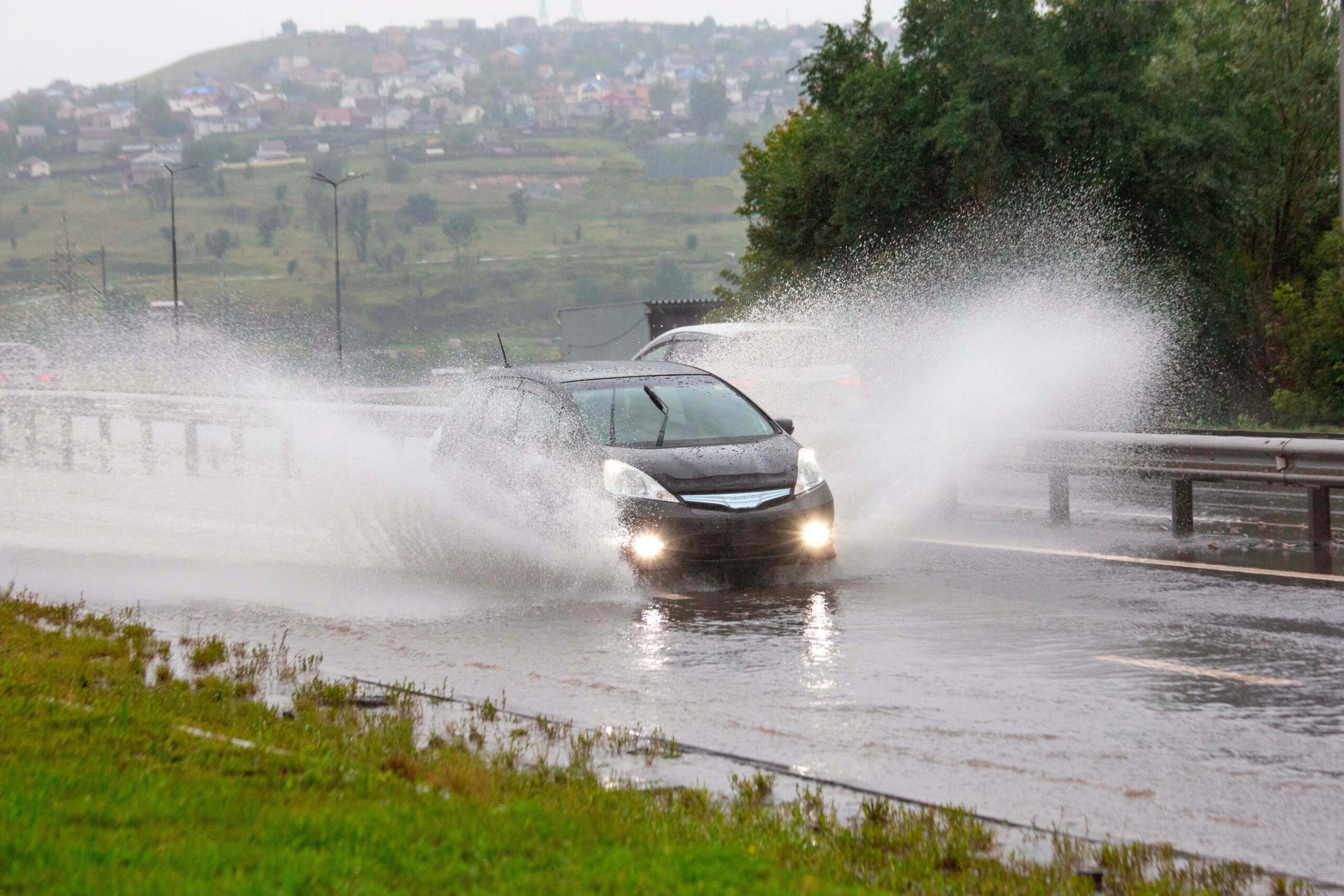 A black car drives through a large puddle on a wet road