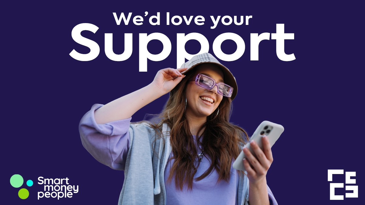 A person wearing a hat and large purple glasses smiles in front of a dark blue background.